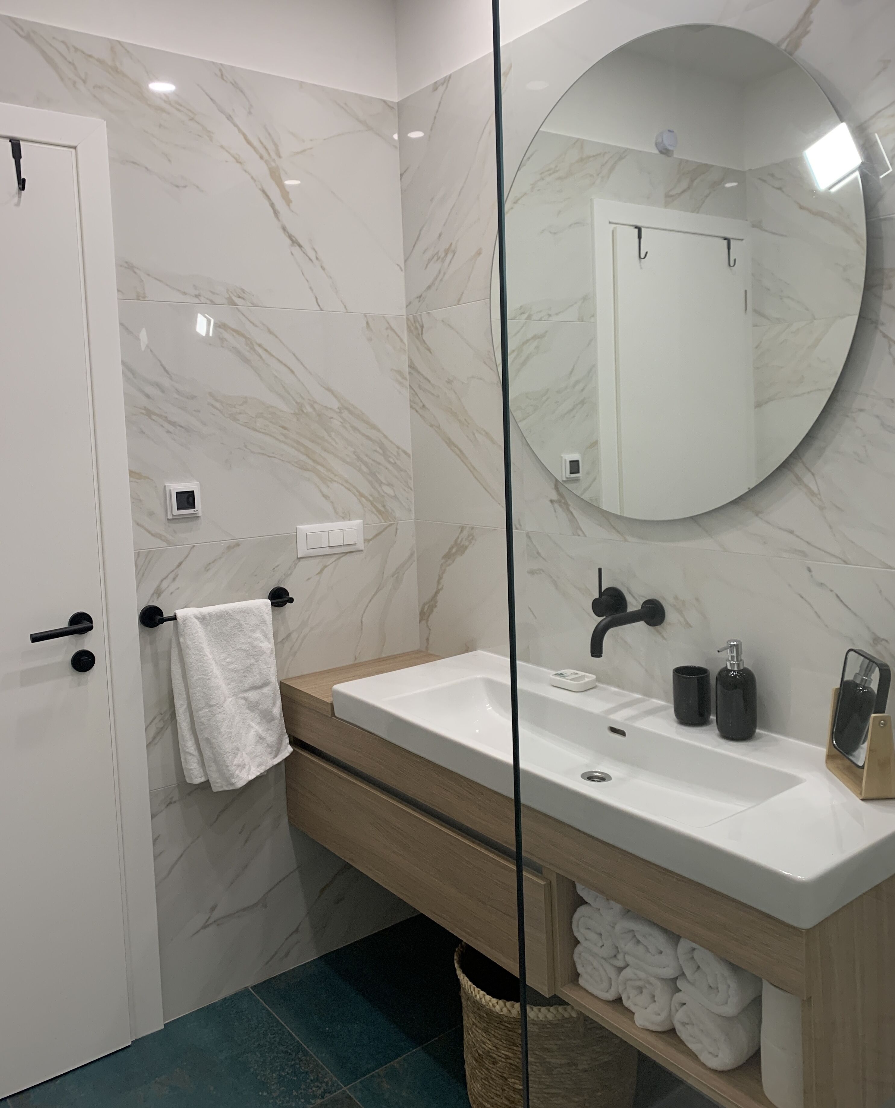 A modern bathroom with a marble wall, a white sink, a mirror, and a towel rack.