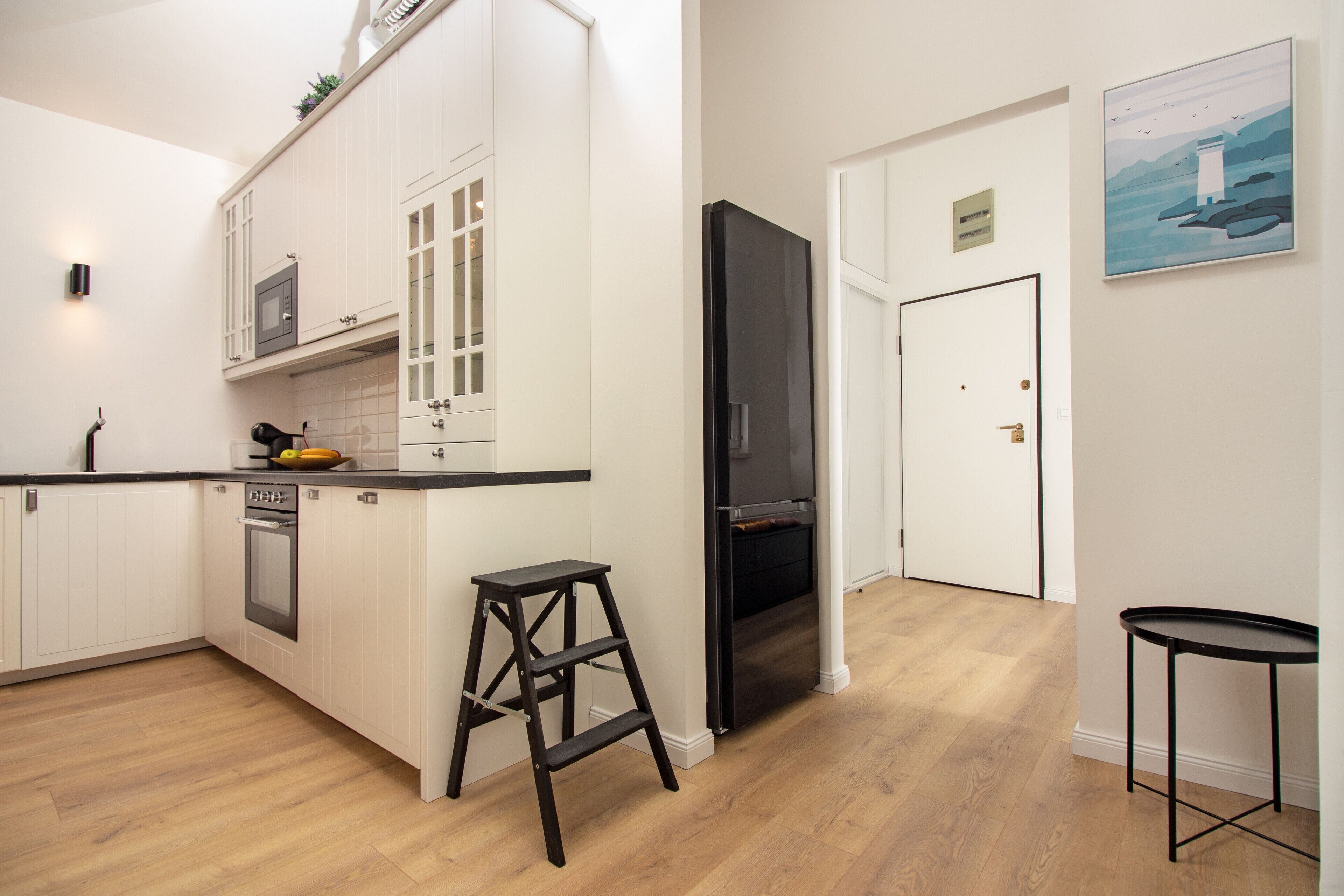 Une cuisine moderne avec des meubles blancs, un réfrigérateur noir et un plancher en bois.