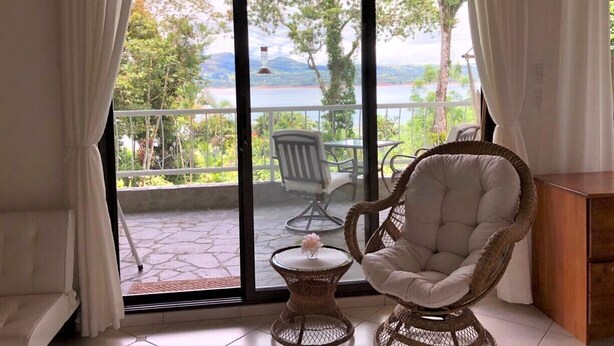 A room with a wicker chair and a small table, a sliding glass door leading to an outdoor area with a chair and a table, and a wooden cabinet.