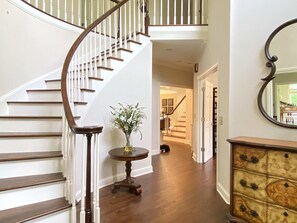 Staircase and elegant mirror adorn this inviting space, complemented by a beautiful wooden table and vase.