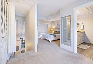 Una camera da letto con un letto, un ventilatore a soffitto, un comodino e un bagno con lavandino e specchio.