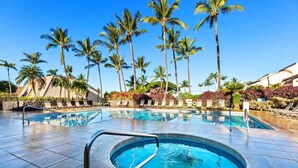 A swimming pool with lounge chairs, palm trees, and a clear blue sky.