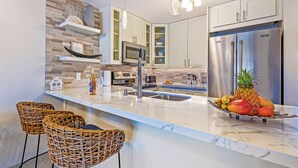 A modern kitchen with white cabinets, a stainless steel refrigerator, and a marble countertop.