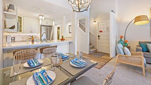 A modern kitchen with a dining area, a staircase, and a living room with a sofa and lamp.