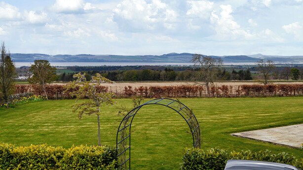 A grassy landscape with a metal arch structure, a distant body of water, and rolling hills. - Grange Loft - UK31594 (Dundee)
