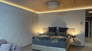 A modern bedroom with a large bed, two bedside lamps, a chandelier, a sofa, and a small side table. - Garden/whirlpool/combination sauna large kitchen, rain shower. Very modern (Habscheid)