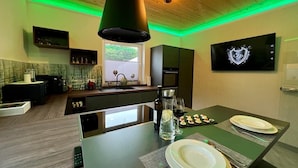 A modern kitchen with a dining area, green ambient lighting, a flat-screen TV, and a wooden ceiling. - Garden/whirlpool/combination sauna large kitchen, rain shower. Very modern (Habscheid)