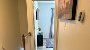 Un couloir doté d’un plancher en bois, un escalier avec une rampe en bois, une console noire ornée d’une plante et un tableau encadré accroché au mur.