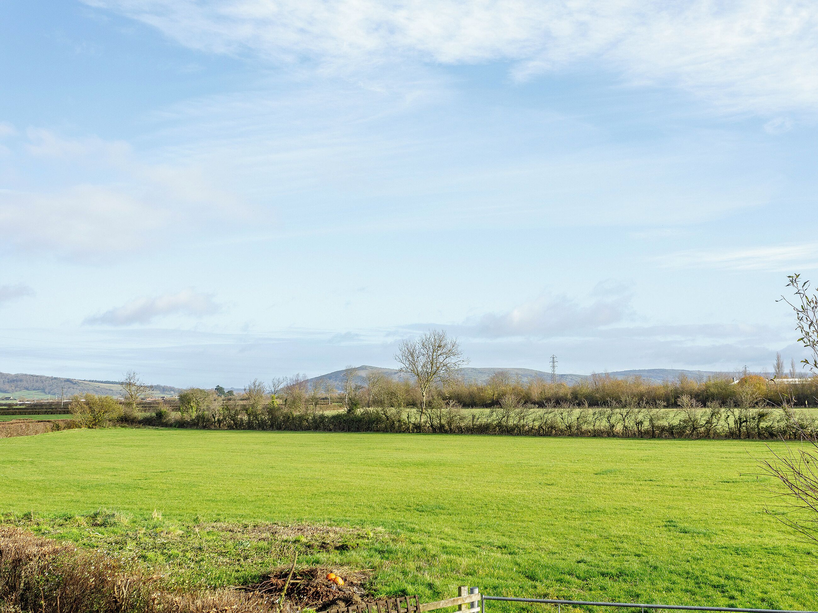Un paysage rural avec un champ verdoyant, une clôture en bois et des collines à l’horizon.