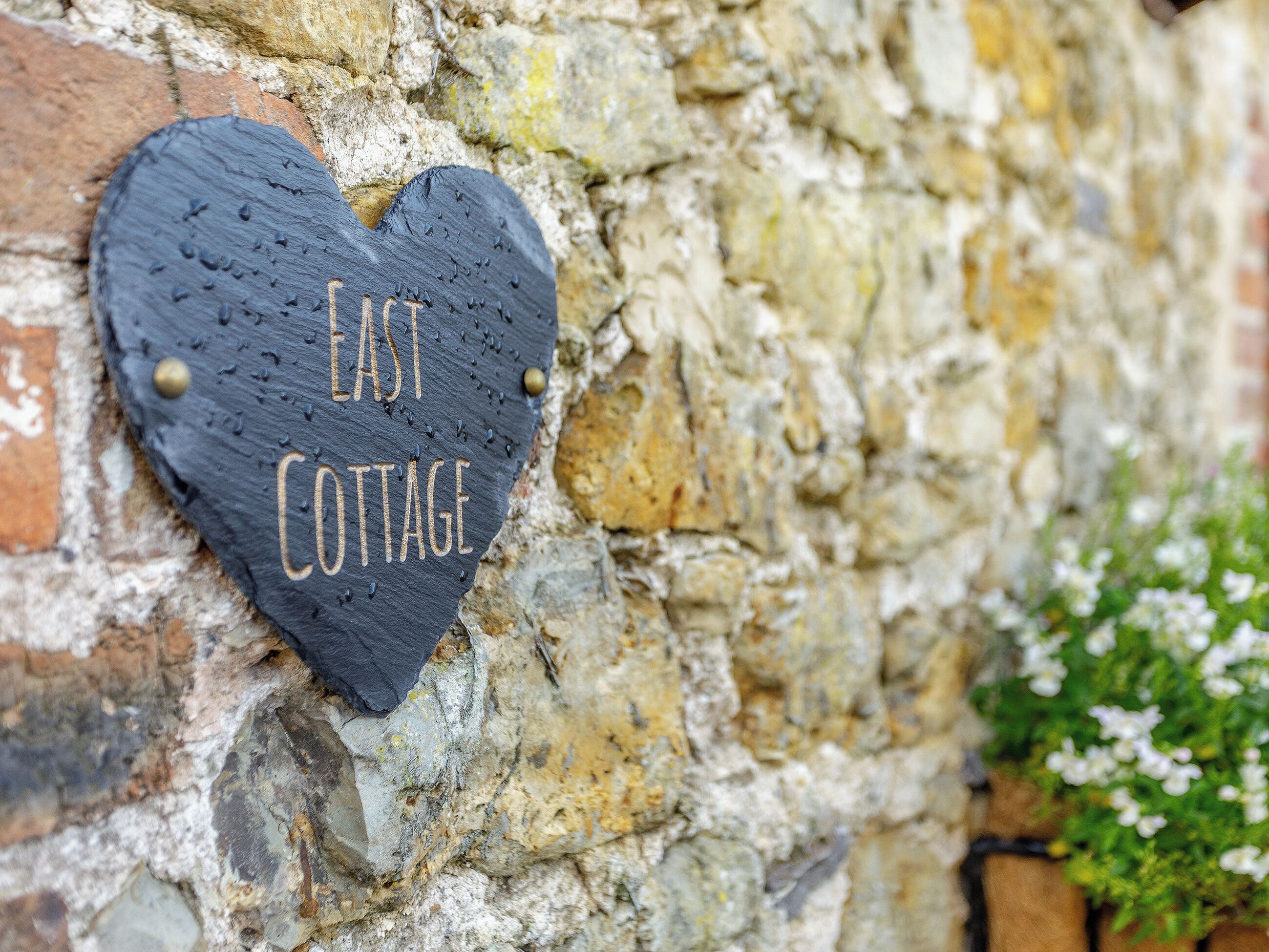 A heart-shaped sign with the words 'EAST COTTAGE' on a stone wall.