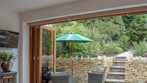 A modern living room with a glass door leading to a patio, wicker furniture, a stone wall, and a staircase. - 1 bedroom accommodation in Harvington, near Evesham (Harvington, near Evesham)