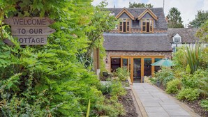 A cottage with a wooden sign, a stone pathway, and a garden. - 1 bedroom accommodation in Harvington, near Evesham (Harvington, near Evesham)