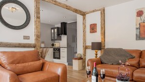 A living room with leather sofas, a wooden coffee table with wine glasses and a bottle, a mirror, and a kitchen in the background. - 1 bedroom accommodation in Harvington, near Evesham (Harvington, near Evesham)