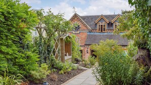 A garden pathway leading to a house with a brick facade, a wooden deck, and a variety of plants. - 1 bedroom accommodation in Harvington, near Evesham (Harvington, near Evesham)