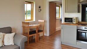 A compact kitchen with a microwave and oven, a dining table with chairs, and a sofa with cushions. - 1 bedroom accommodation in Alkham, near Dover (Alkham, near Dover)
