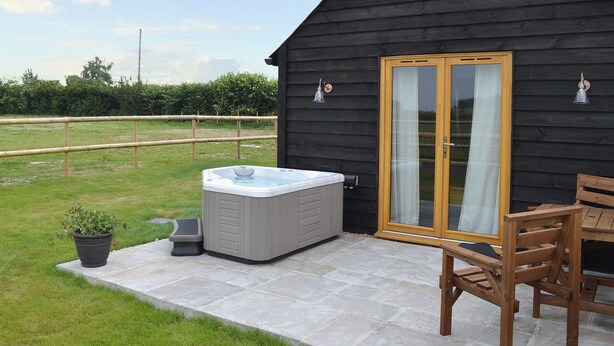 A wooden cabin with a hot tub, a wooden chair, and a glass door. - 1 bedroom accommodation in Alkham, near Dover (Alkham, near Dover)