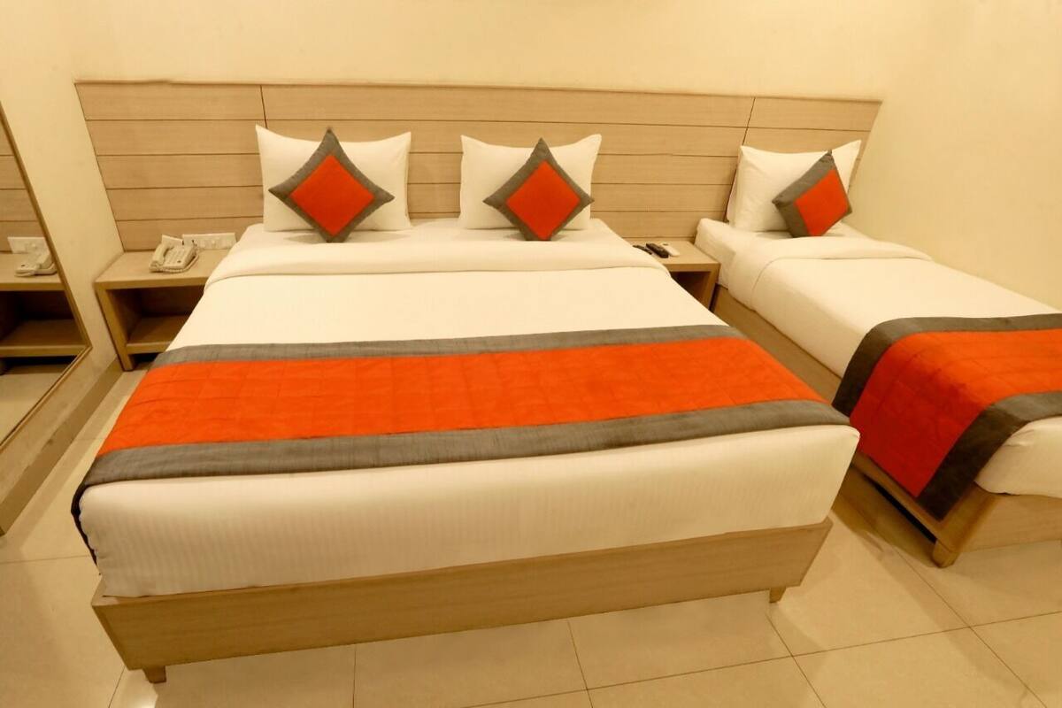 A hotel room with two beds, each with a wooden headboard, white bedding, and orange and gray accent pillows.
