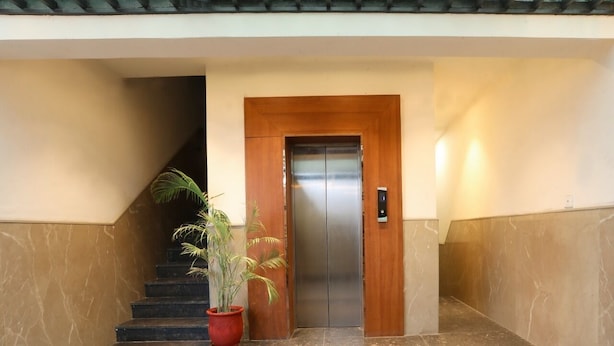 A modern elevator with a wooden frame and a metallic door, flanked by marble walls and a potted plant. - Sagar Residency (Amritsar)