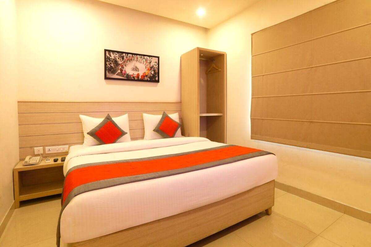 A modern hotel room with a large bed, a bedside table with a phone, and a wardrobe.