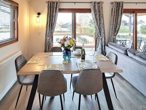 A dining area with a table set for four, a vase of flowers, and a view of the outside. - Perfect water’s edge holiday accommodation, set in a quiet marina. (Brundall)