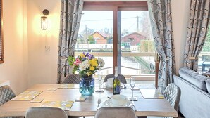 A dining area with a table set for two, a vase with flowers, and a bottle of wine.