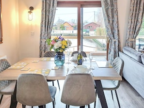 A dining area with a table set for two, a vase with flowers, and a bottle of wine.