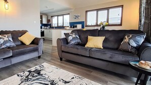 A living room with two sofas, a coffee table, and a rug. There is a kitchen in the background.