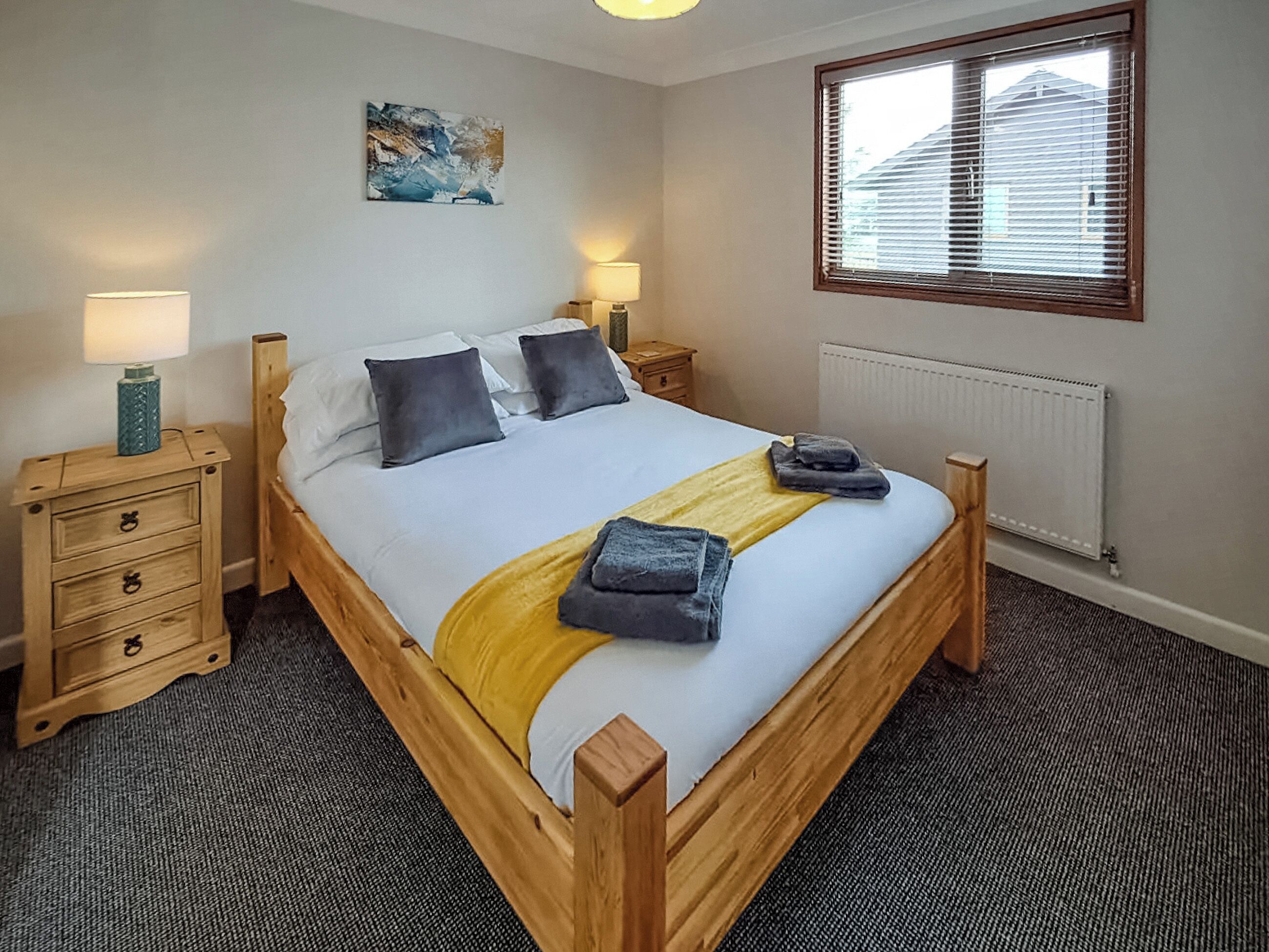 A bedroom with a wooden bed, two bedside tables, a radiator, and a window with blinds.