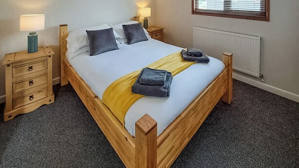 A bedroom with a wooden bed, two bedside tables, a radiator, and a window with blinds.
