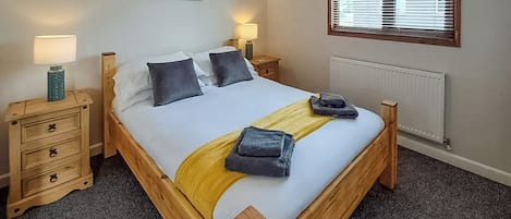 A bedroom with a wooden bed, two bedside tables, a radiator, and a window with blinds.