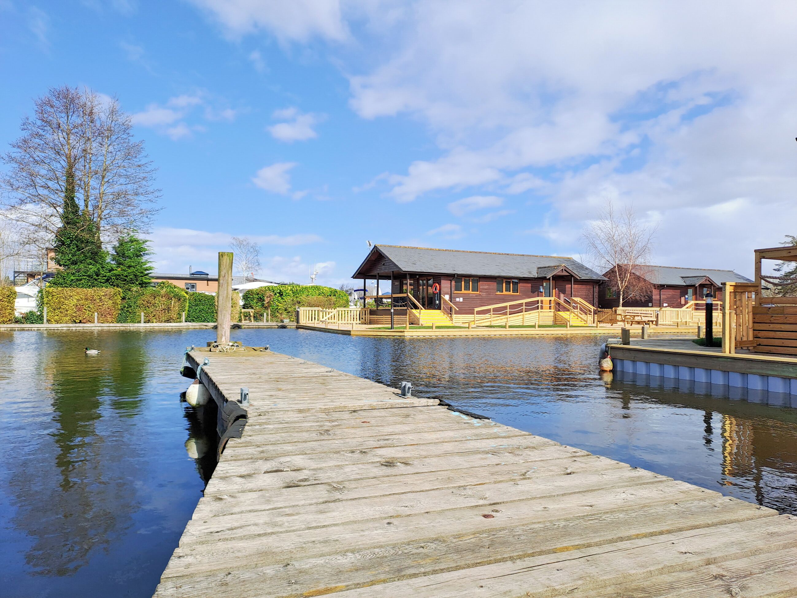 A wooden dock extending into calm water, a wooden building with a porch, and a clear sky.