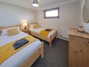 A hotel room with two wooden beds, a nightstand with a lamp, a radiator, and a window with blinds.