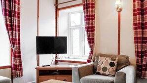 Huoneessa on televisio puupöydällä, kuviollinen koristetyyny sohvan päällä ja punavalkoruutuiset verhot.