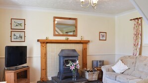 A cozy living room with a fireplace, a television on a wooden stand, a sofa, and a decorative mirror above the fireplace.