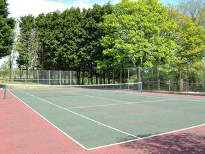 Tenniskenttä, jossa on verkko, ja jonka ympärillä on puita ja aita.