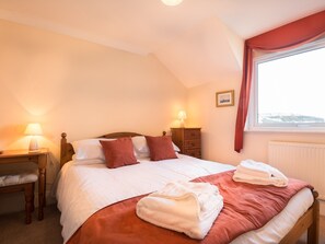 A neatly made bed with pillows, a bedside table with a lamp, a dresser, and a window with curtains. - Marina views from this stunning apartment. (Brixham)