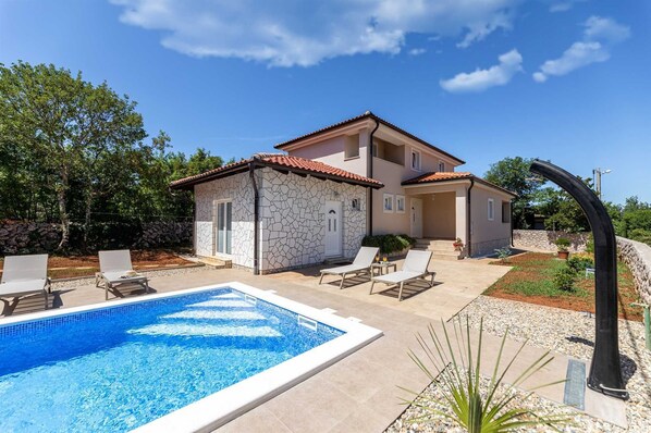 A two-story house with a swimming pool, outdoor seating, and a stone facade.