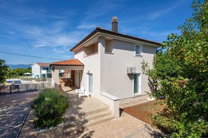 A two-story house with a tiled roof, a covered patio with outdoor furniture, and a view of the sea.