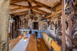Un interior rústico con chimenea de piedra, vigas de madera y diversas herramientas y artefactos.
