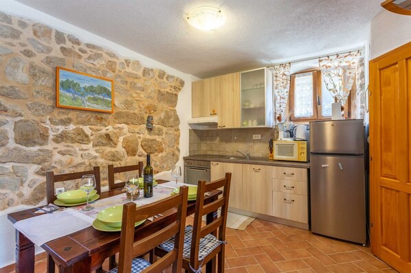 A compact kitchen with stone walls, wooden cabinets, a dining table with chairs, and a refrigerator.