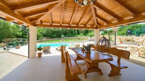 A wooden gazebo with a table and benches, overlooking a swimming pool and garden. - Beautiful Villa Green Pearl with heated pool (Gostinjac (Krk))