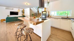 A modern kitchen with a central island, bar stools, a built-in oven, and a window with a view. - Beautiful Villa Green Pearl with heated pool (Gostinjac (Krk))