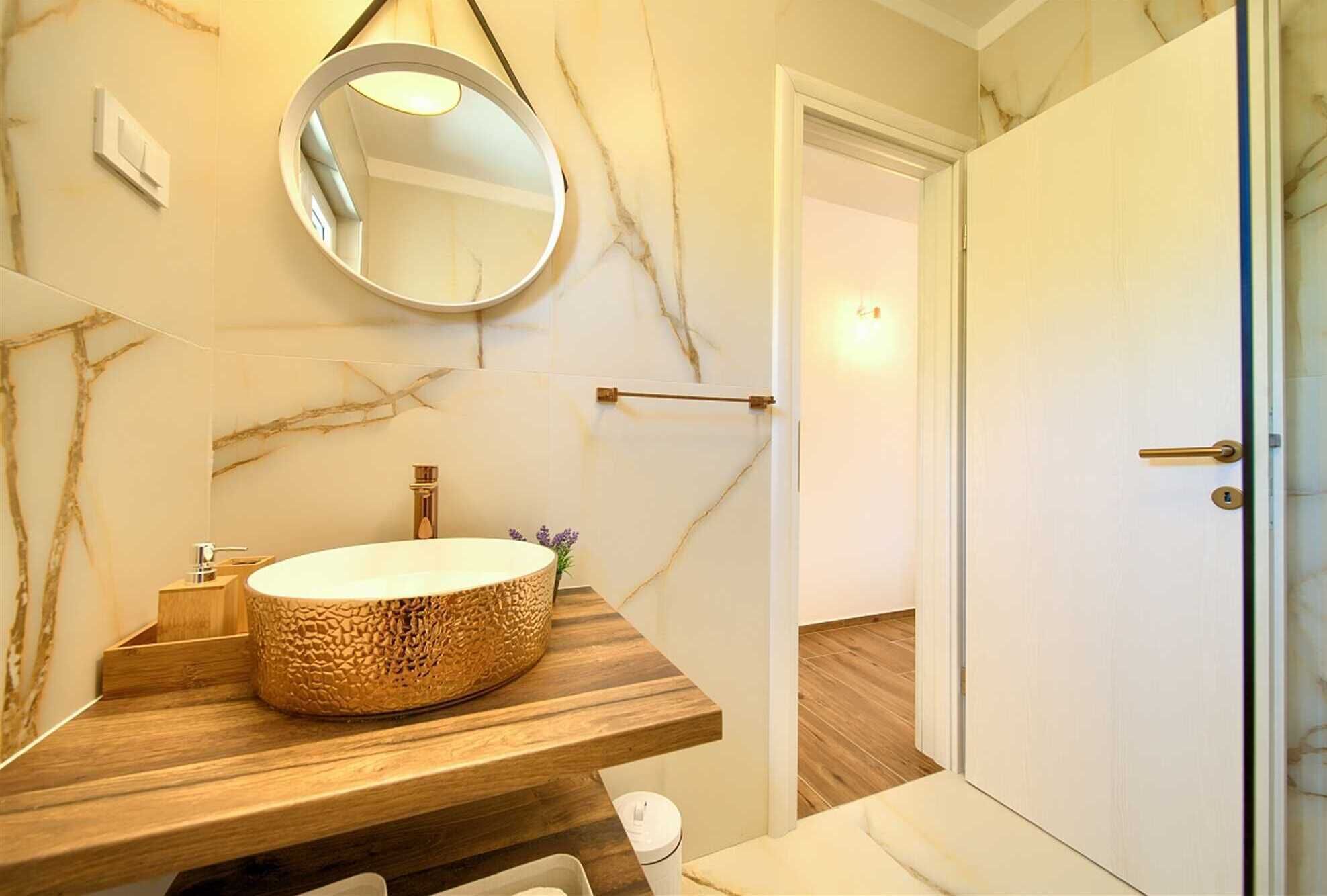 A bathroom with a marble wall, a wooden vanity, a round sink, a mirror, and a door.