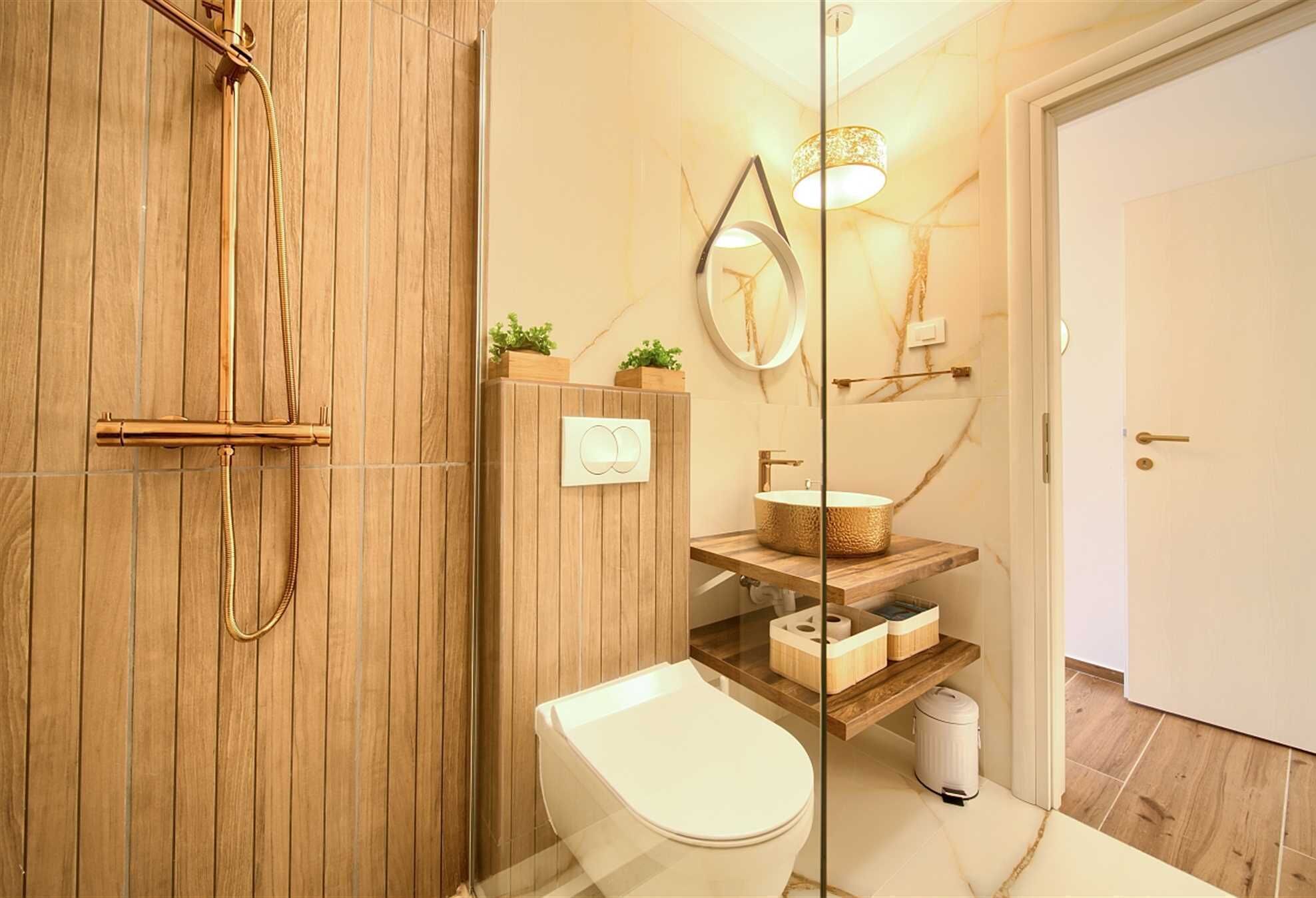 A modern bathroom with a wooden shower enclosure, a white toilet, a wooden vanity with a woven basket sink, and a mirror with a light fixture.