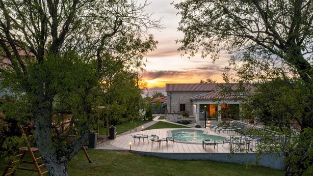 Propiedad residencial con piscina, mobiliario exterior y un edificio de piedra.