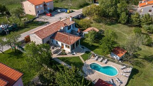 Una propiedad residencial con piscina, un patio cubierto y una casa grande con techo de tejas rojas.