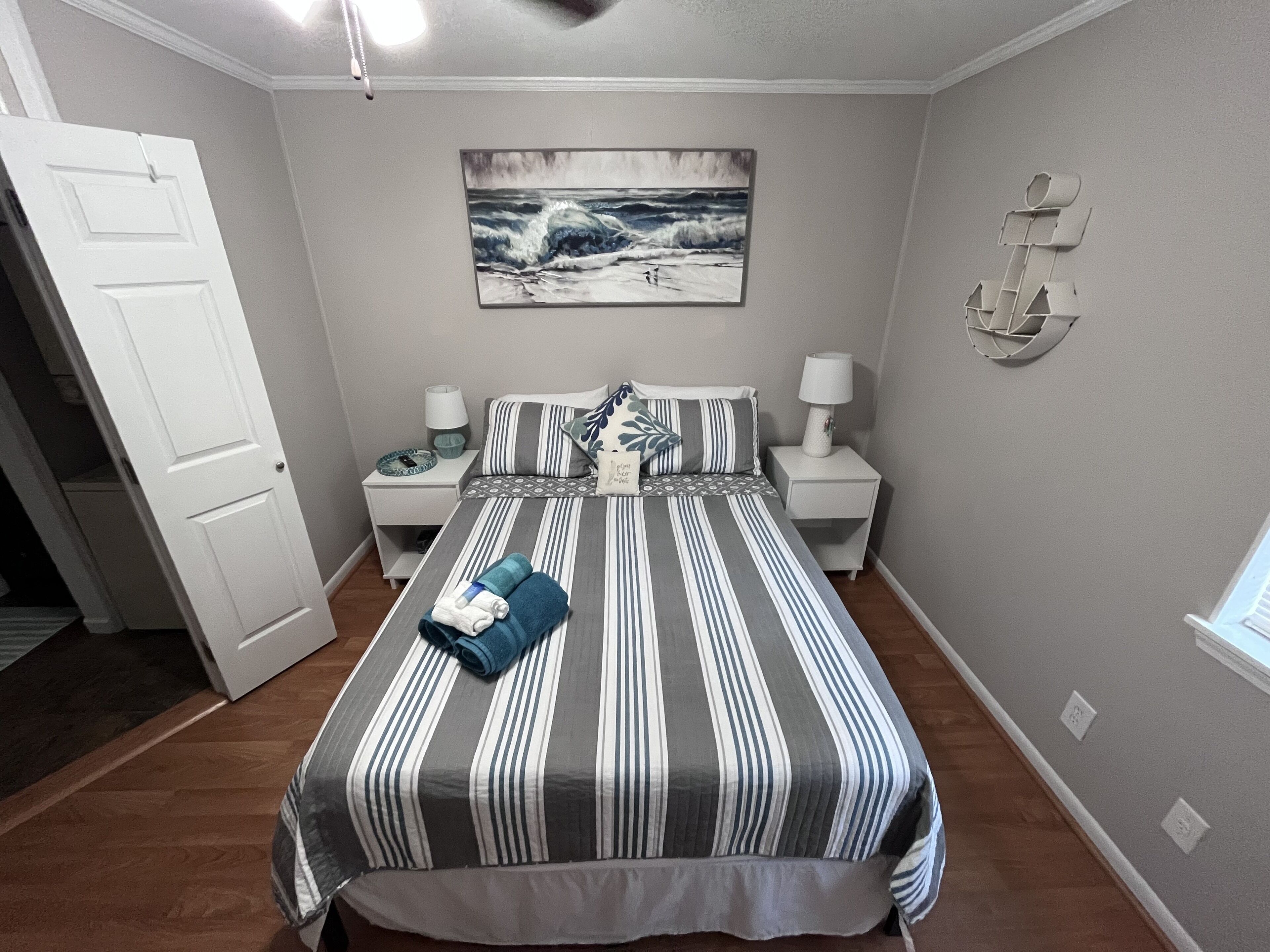 Une chambre à coucher comprenant un lit, deux tables de chevet, une commode, une lampe fixée au mur, un tableau et une porte.