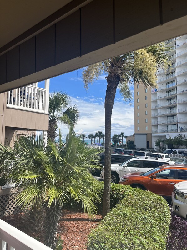 A view of a parking lot with several cars, palm trees, and a building with balconies.