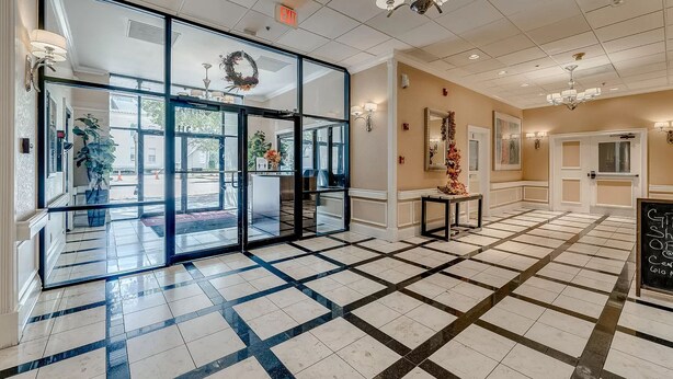 A hotel lobby with a checkered floor, glass entrance doors, a reception desk, and a chandelier.
