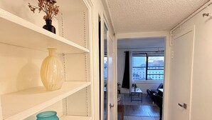 A hallway with white shelves, a teal vase, and a view of a living room through a doorway.